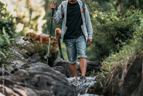 Hikers walk on rocks with dog in the stream flowing from the waterfall.