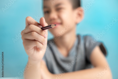 Asian Boy holding a pencil drawing in the air, imagination concept of a child on a blue background