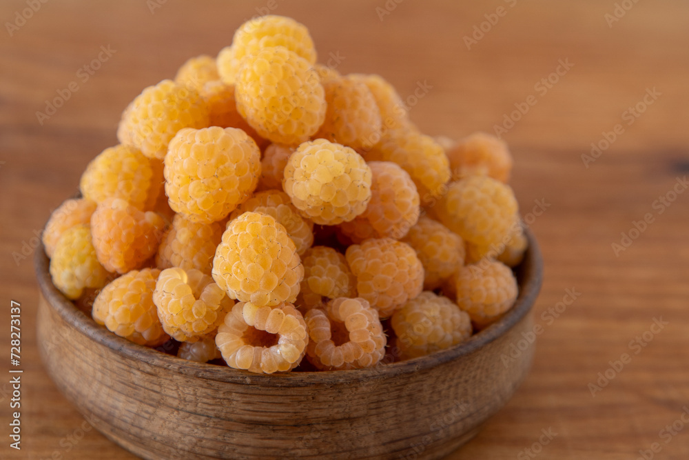 Yellow raspberries in a wooden bowl on the table. Summer berries background. Vitamin food, berry harvest. Healthy nutrition. Yellow raspberries in a wooden bowl on the table. Summer berries background. Vitamin food, berry harvest. Healthy nutrition.