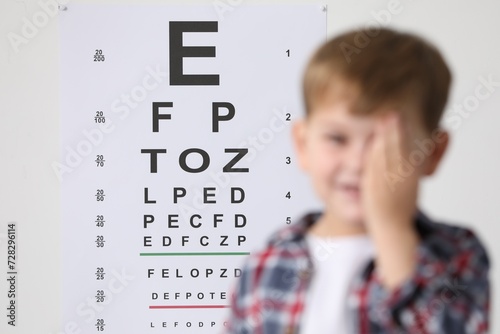 Little boy covering her eye against vision test chart, selective focus