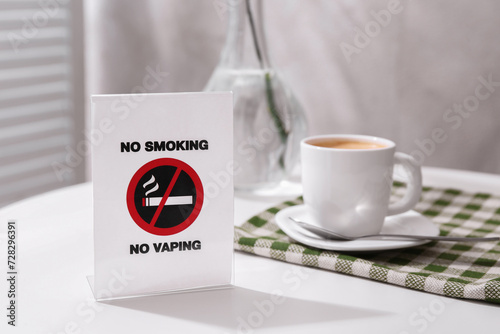 No Smoking No Vaping sign and cup of coffee on white table indoors