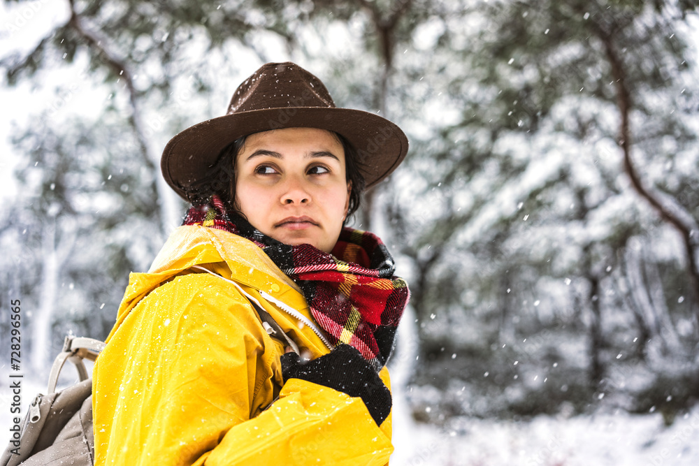 Fototapeta premium Young woman with yellow rain coat hiking in the forset on a snowy day