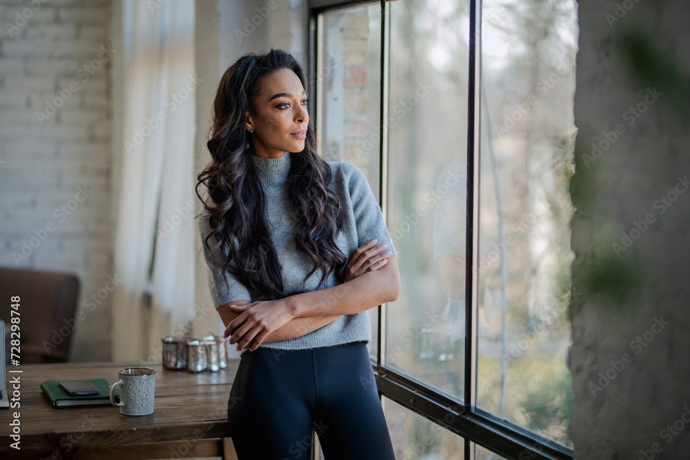 An Afro-American woman standing with arms crossed and the window and looking thoughtfully An Afro-American woman standing with arms crossed and the window and looking thoughtfully