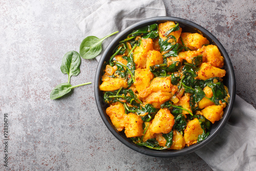Saag aloo is a classic Indian style side dish featuring potatoes fried in spices and spinach closeup on the bowl on the table. Horizontal top view from above