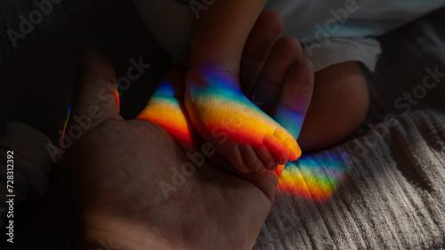 A man holds his newborn son by the leg. Beam of light through a prism.  photo