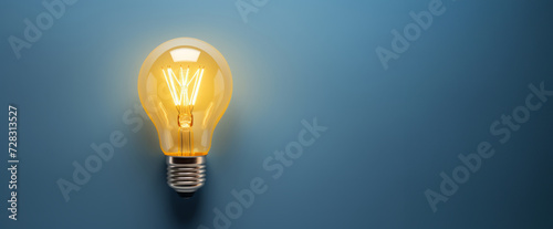 Glowing light bulb on plain blue background symbolizing ideas photo