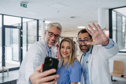 Portrait of doctors and nurse standing in hospital corridor. Healthcare workers in modern private clinic, taking selfie, smiling.