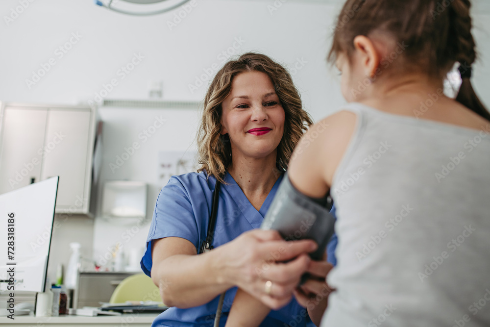 Doctor examining young girl, measuring blood pressure, using medical blood pressure monitor. Concept of preventive health care for children.
