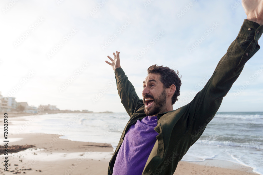 Carefree man enjoying with arms raised at beach