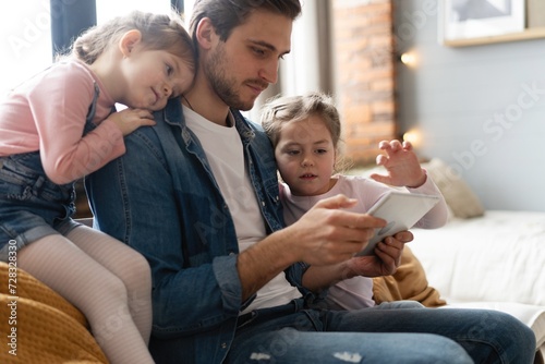 Image of happy young father and two daughters sitting on sofa with tablet.