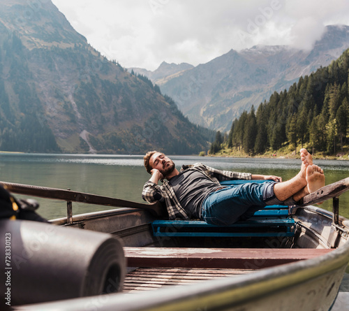 Young man relaxing in boat at lake Vilsalpsee near mountains, Tyrol, Austria