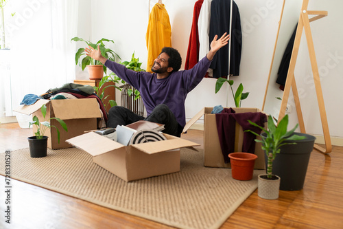 Cheerful young man with arms raised organizing and decluttering at home photo