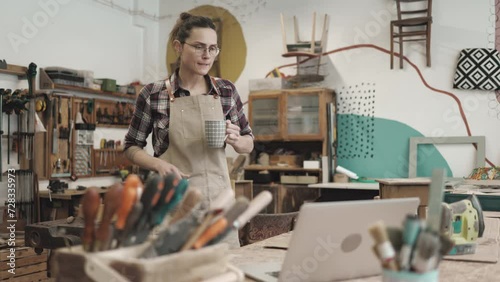 Female carpenter drinking coffee and using laptop in her workshop
 photo