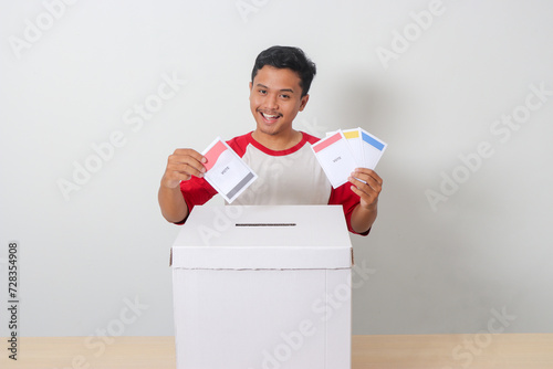 Portrait of excited Asian man inserting and putting the voting paper into the ballot box. General elections or Pemilu for the president and government of Indonesia. Isolated image on white background photo