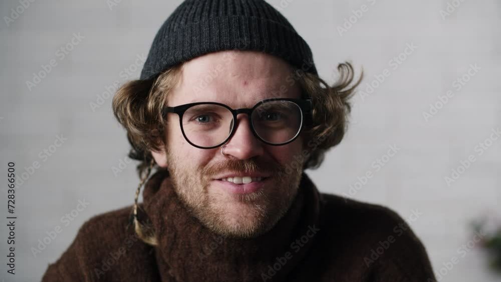 European man in stylish eyeglasses blinking his blue eyes. Mid shot guy staying in office. Headshot of caucasian guy with curly hair in hat. A professional actor European man in stylish eyeglasses blinking his blue eyes. Mid shot guy staying in office. Headshot of caucasian guy with curly hair in hat. A professional actor