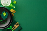 Celebrate in style at the pub for St. Patrick's: top view black plate, napkin holding knife and fork, beer glass, gold coins, trefoils, confetti, and beads displayed on a vivid green setting