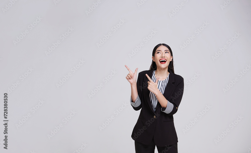 portrait of an attractive asian businesswoman in suit standing with presenting or showing hand pointing finger to copy space for product isolated on gray background. portrait of an attractive asian businesswoman in suit standing with presenting or showing hand pointing finger to copy space for product isolated on gray background.