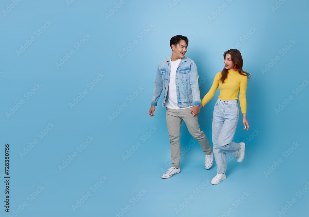 Obraz premium Full body smiling happy young Asian teen couple holding hands and walking together isolated on blue copy space studio background.