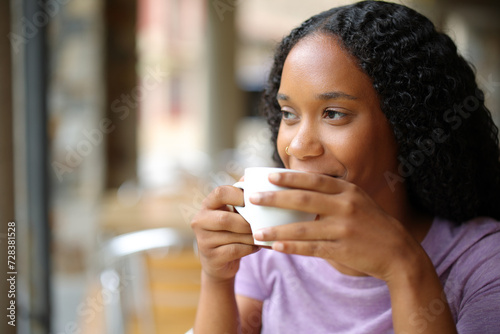 Satisfied black woman drinking coffee in a terrace photo