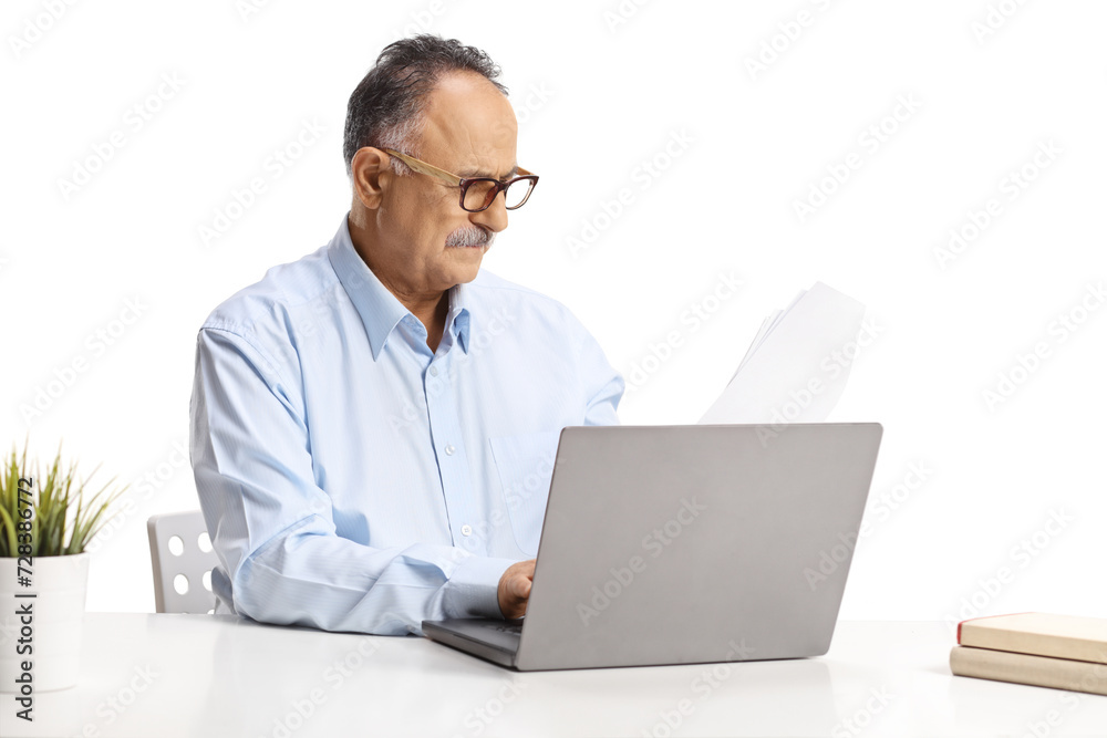 Mature man sitting at a desk and working on a laptop computer Mature man sitting at a desk and working on a laptop computer