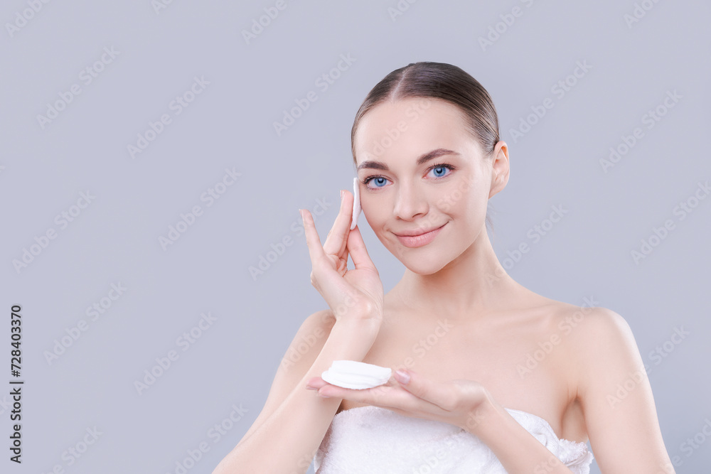 Beautiful woman cleaning her face with cotton swab over background and smiling Beautiful woman cleaning her face with cotton swab over background and smiling