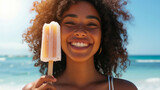 Portrait of a young smiling African American woman eating a popsicle ice cream on hot summer day at the beach