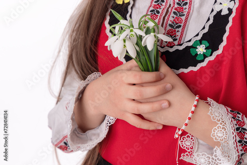 Bulgarian girl in ethnic folklore embroidery dress nosia, yarn bracelet martenitsa, and spring bouquet snowdrops symbol of Bulgaria