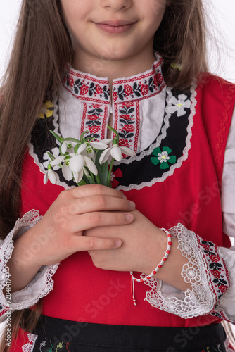 Bulgarian girl in traditional folklore costumes with spring flower bouquet snowdrops and handcraft wool bracelet martenitsa symbol of Baba Marta and march photo