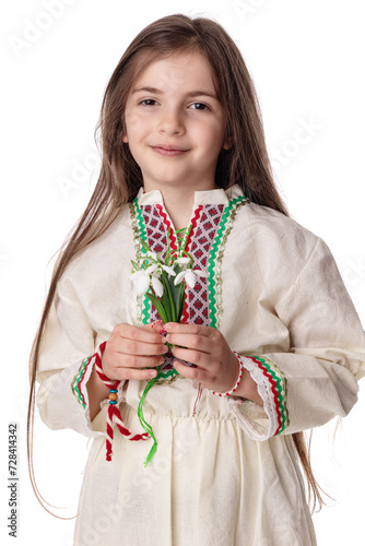 Bulgarian girl with snowdrops spring flowers bouquet wearing traditional ethnic folklore dress and white red yarn bracelet martenitsa martisor, Bulgaria