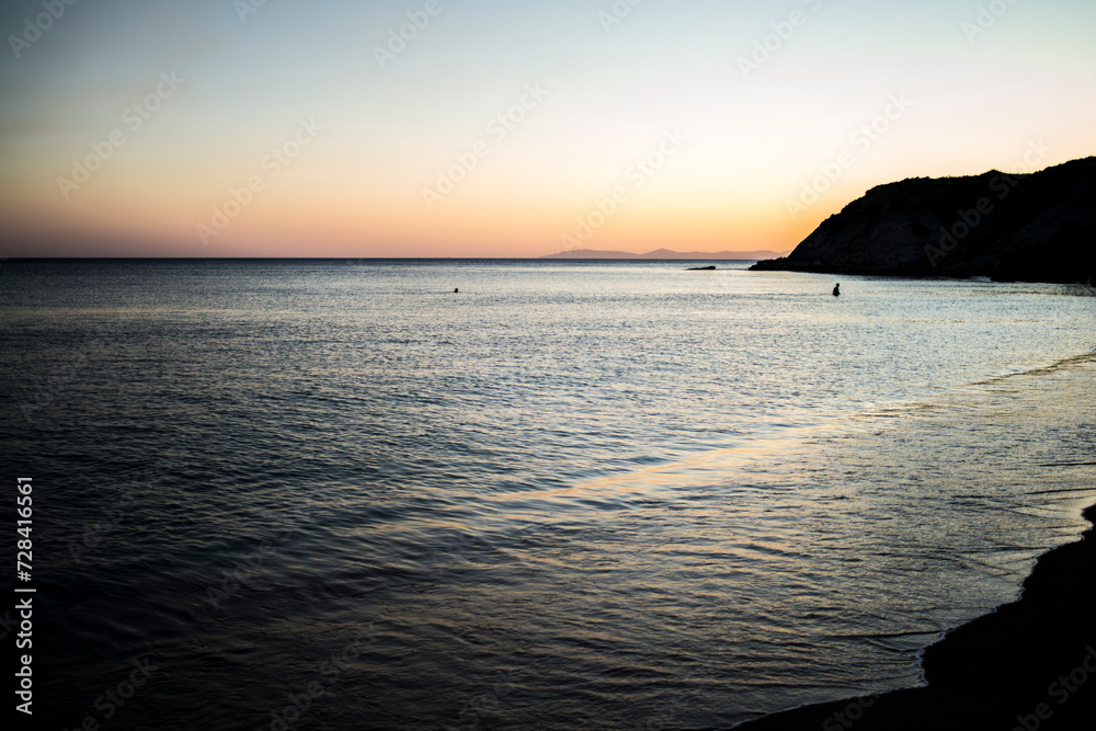 A tranquil scene as people enjoy a sunset swim in the calm sea, bathed in the warm hues of dusk, creating a serene coastal atmosphere.