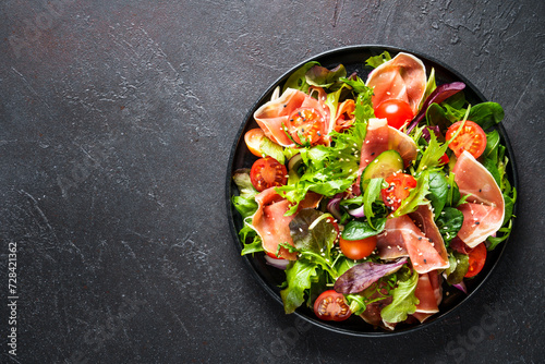 Salad in black bowl at dark background.