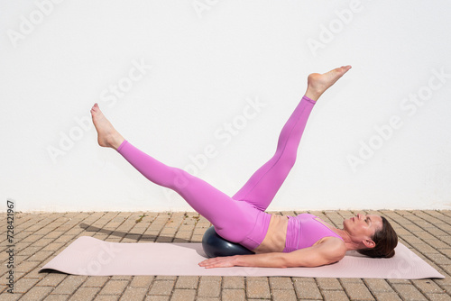 fit sporty woman doing pilates ball exercises outside. scissor stretch for legs