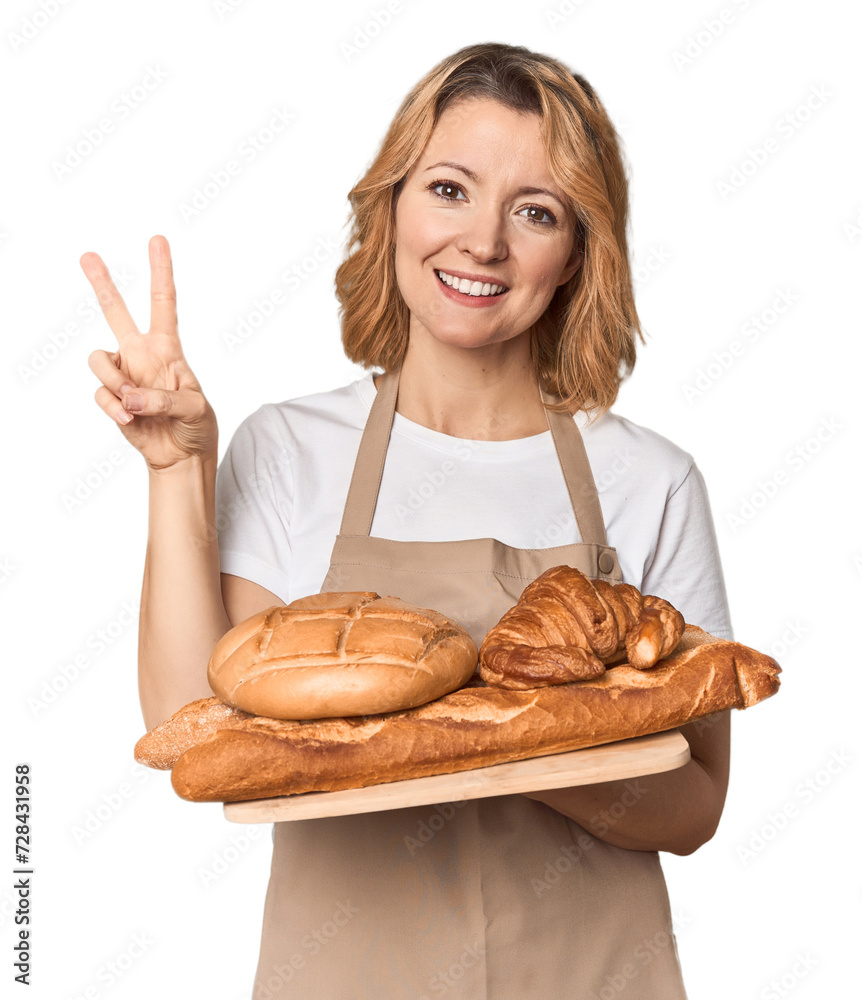 Middle-aged Caucasian woman baker with bread tray joyful and carefree showing a peace symbol with fingers. Middle-aged Caucasian woman baker with bread tray joyful and carefree showing a peace symbol with fingers.