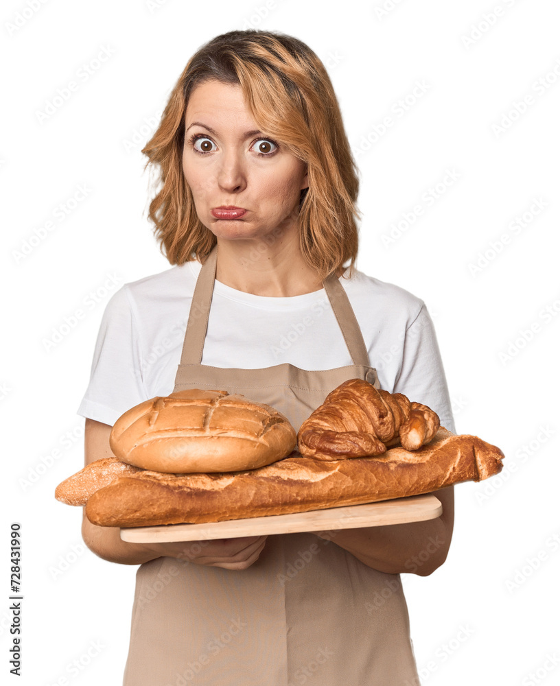Middle-aged Caucasian woman baker with bread tray confused, feels doubtful and unsure. Middle-aged Caucasian woman baker with bread tray confused, feels doubtful and unsure.