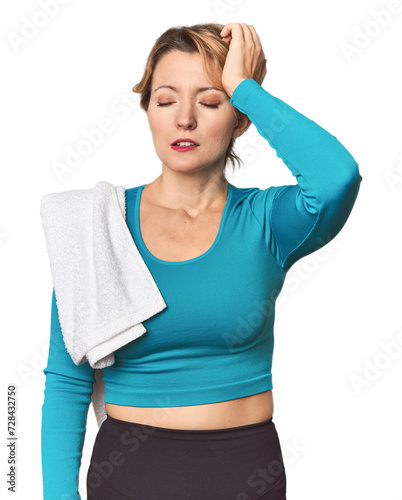 Caucasian woman in sportswear with towel tired and very sleepy keeping hand on head.