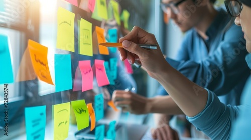 In an office setting, business people gather for meetings, engaging in collaborative activities such as writing memos on sticky notes. The focus is on planning strategies, brainstorming ideas