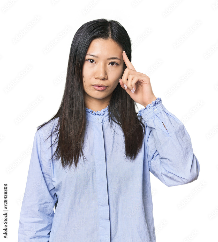 Young Chinese woman in blue shirt pointing temple with finger, thinking, focused on a task. Young Chinese woman in blue shirt pointing temple with finger, thinking, focused on a task.