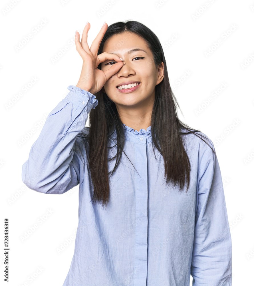 Young Chinese woman in blue shirt excited keeping ok gesture on eye. Young Chinese woman in blue shirt excited keeping ok gesture on eye.