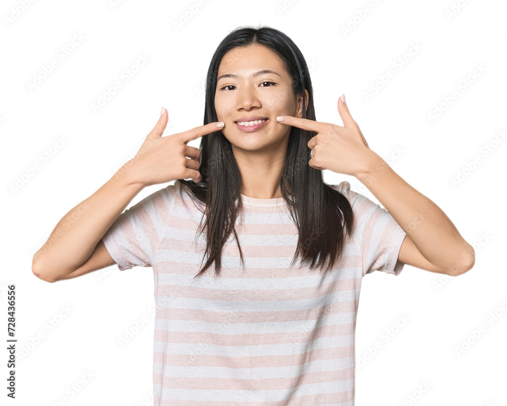 Young Chinese woman in studio setting smiles, pointing fingers at mouth. Young Chinese woman in studio setting smiles, pointing fingers at mouth.