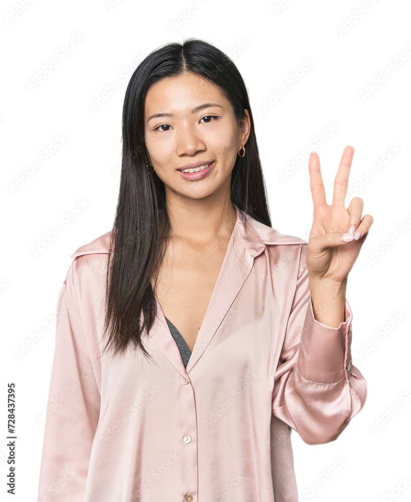 Young Chinese woman in studio setting joyful and carefree showing a peace symbol with fingers. Young Chinese woman in studio setting joyful and carefree showing a peace symbol with fingers.