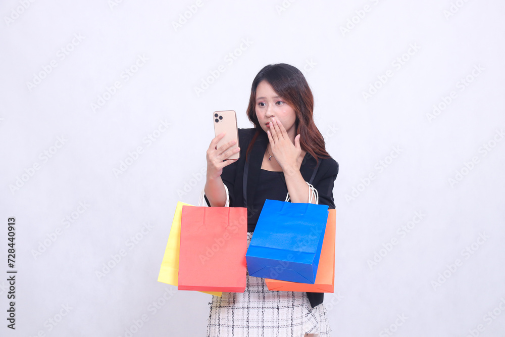 Beautiful Asian girl 20s formal office customer in shock looking at cellphone covering mouth while carrying shopping paper bag isolated on white background Beautiful Asian girl 20s formal office customer in shock looking at cellphone covering mouth while carrying shopping paper bag isolated on white background