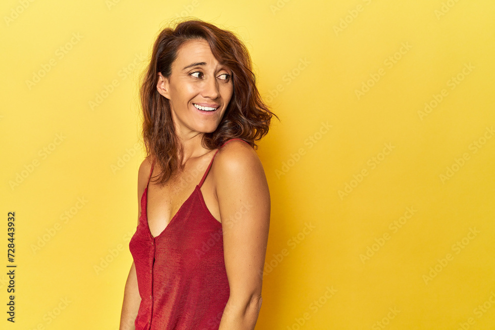 Middle-aged woman on a yellow backdrop looks aside smiling, cheerful and pleasant. Middle-aged woman on a yellow backdrop looks aside smiling, cheerful and pleasant.