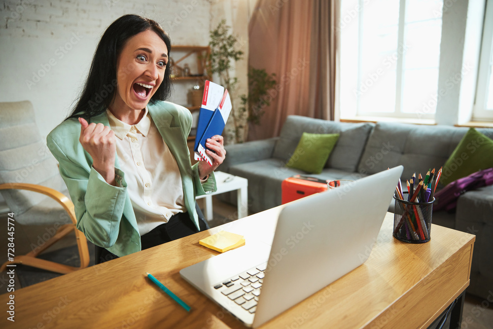 Happy, emotional businesswoman sitting in her office, talking on video call and showing plane tickets. Long awaited vacation. Concept of traveling, online services for booking, tourism, vacation Happy, emotional businesswoman sitting in her office, talking on video call and showing plane tickets. Long awaited vacation. Concept of traveling, online services for booking, tourism, vacation