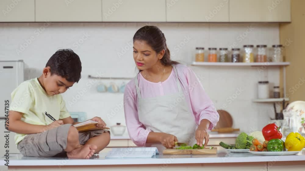 Indian working mother at kitchen helping her kid or child to do homework - concept of multitasking, parenthood and family responsibility Indian working mother at kitchen helping her kid or child to do homework - concept of multitasking, parenthood and family responsibility