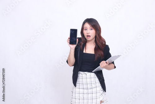 Beautiful Indonesian woman in her 20s, formal office, surprised to see a black cellphone gadget and carrying a tablet for promotion isolated on a white background