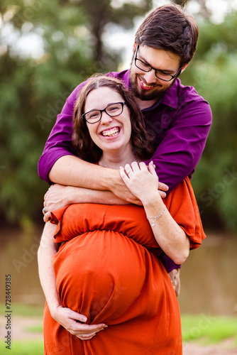 Happy expectant couple husband holding wife with her arm on pregnant belly photo