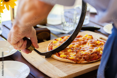 Man cutting home made pizza for family lunch on outdoor table photo