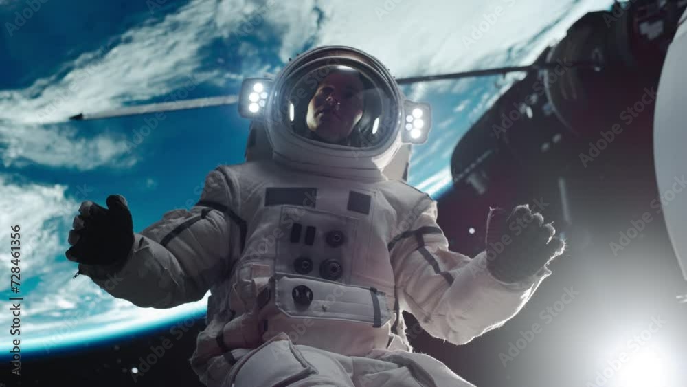 Portrait of a Young Male Astronaut Posing in a Space Suit During a Spacewalk Outside a Spaceship, Satellite or a Space Station. Spaceman Looking at Camera, Smiling and Waving Hello Gesture with Hand