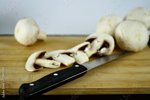 whole and folk champignons on a wooden board and a knife lies nearby