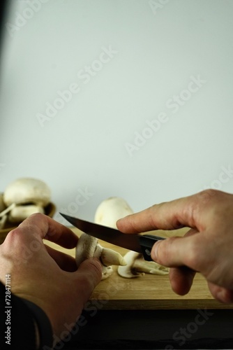 Male hands cutting champignons on a wooden board